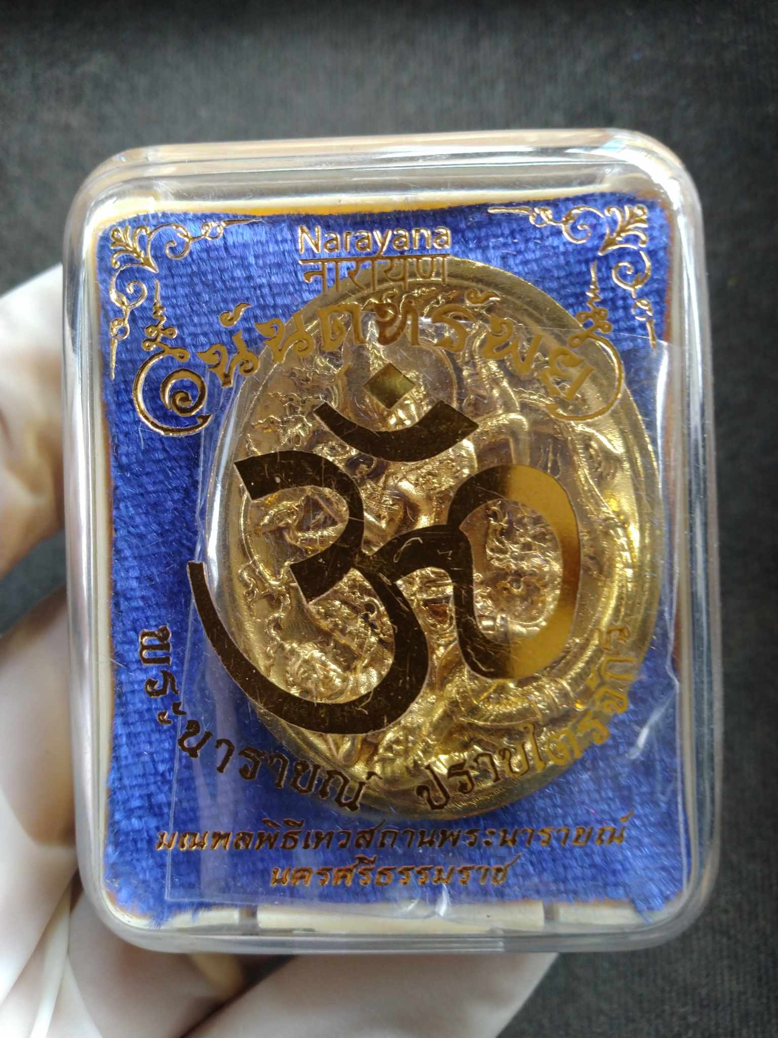 Narai the Great amulet gold medallion with embossed deity design in clear plastic display case with blue backing