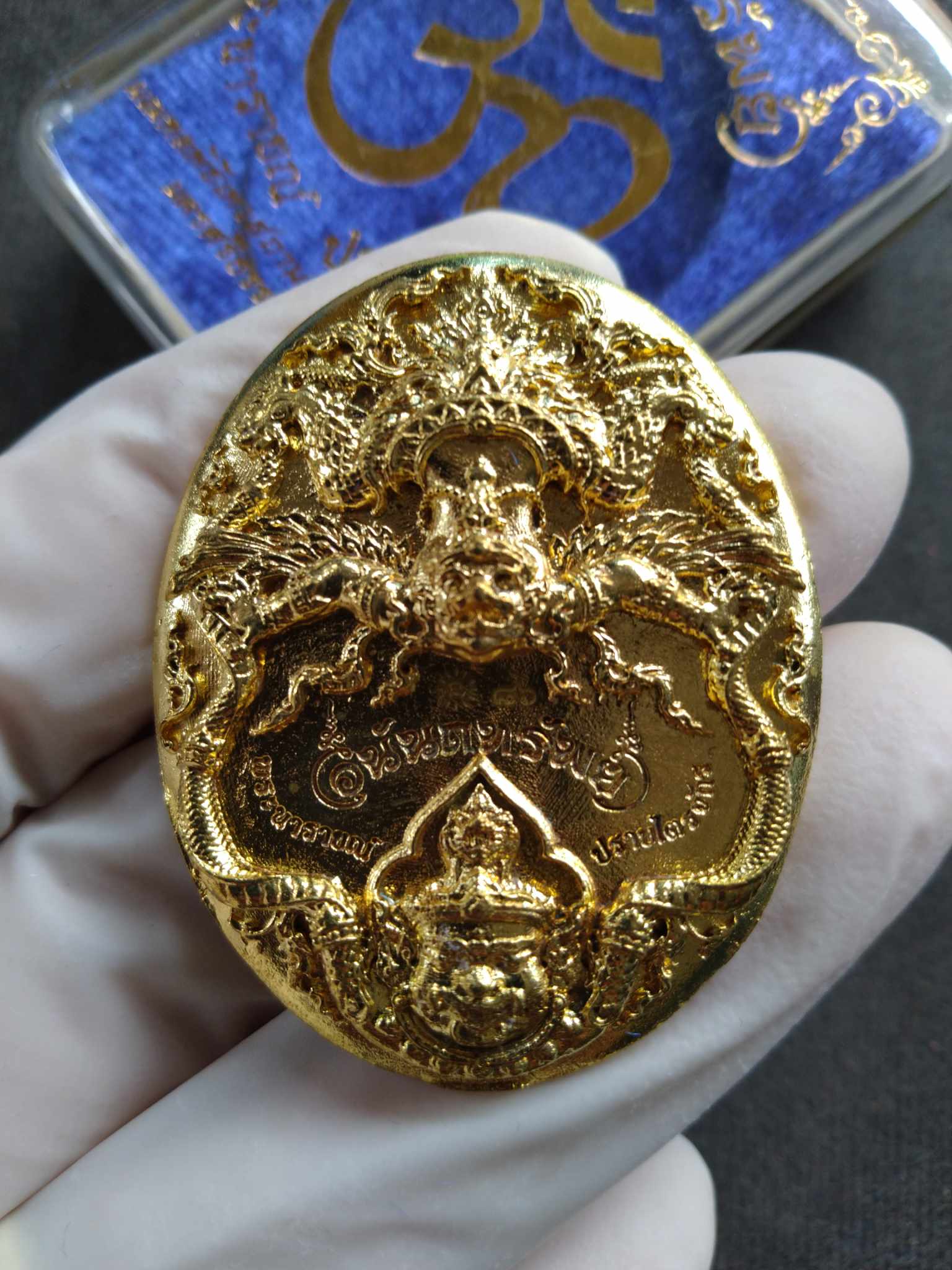 Hand holding ornate gold Narai the Great amulet with intricate deity and mythic dragon details on display