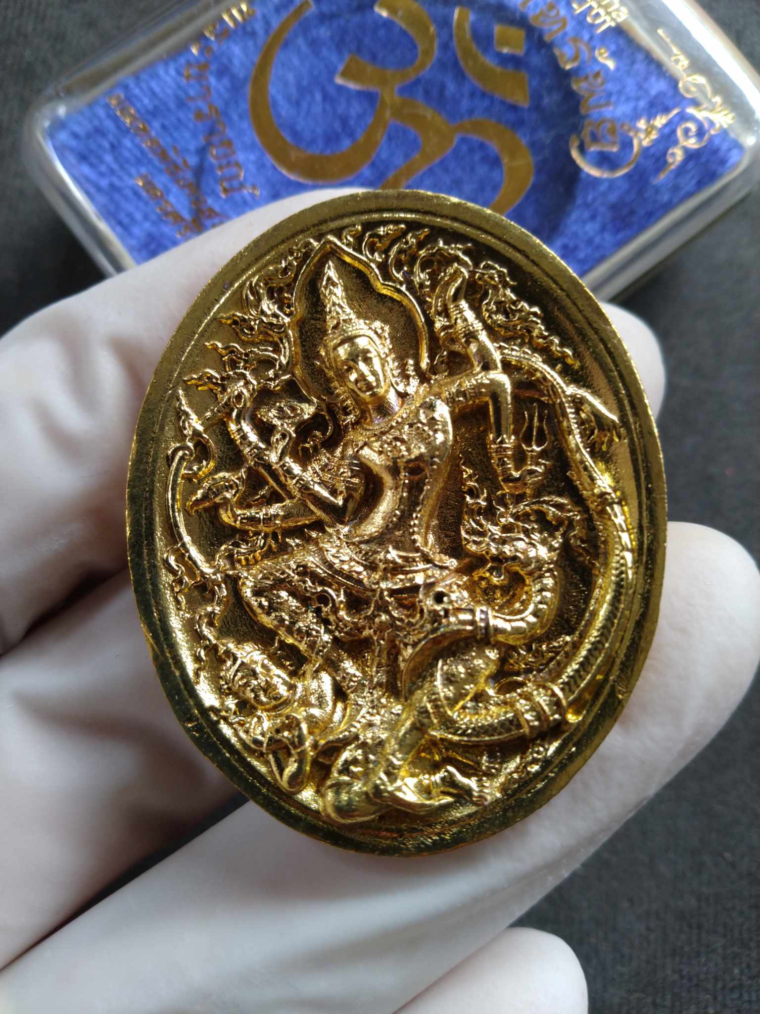 Narai the Great amulet gold oval Thai deity intricate relief held in gloved hand by Thai Blessing Co