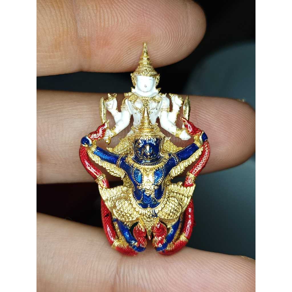 Narayana on Garuda amulet held between fingers with intricate gold, red, and blue details
