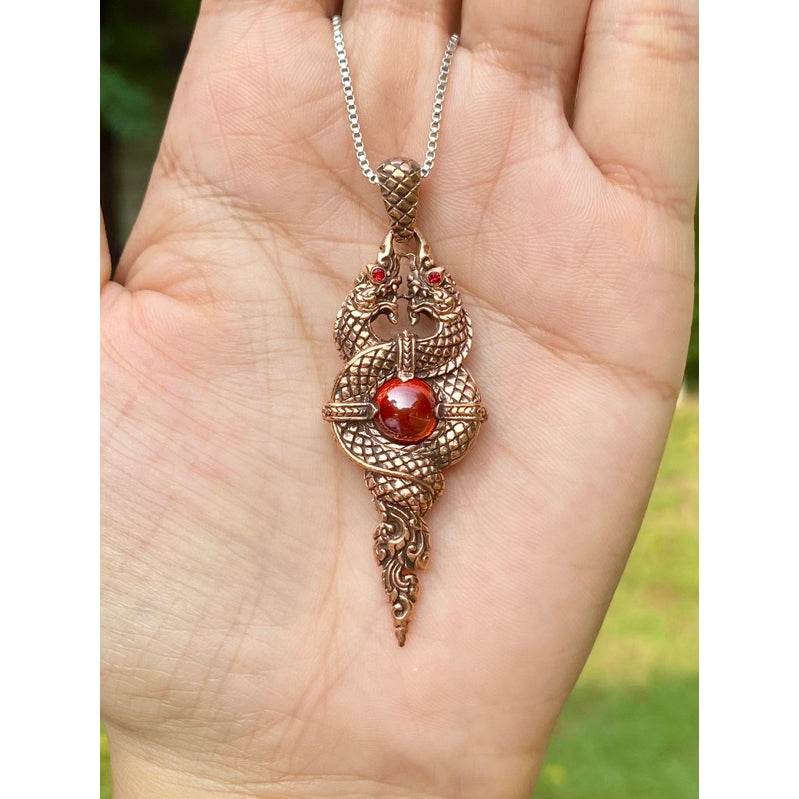 Naga wealth elevation amulet copper pendant with red stone on chain held in palm by Thai Blessing Co
