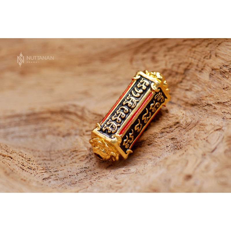 Thai billionaire takrud amulet gold cylinder with black and red script engraving on wooden background