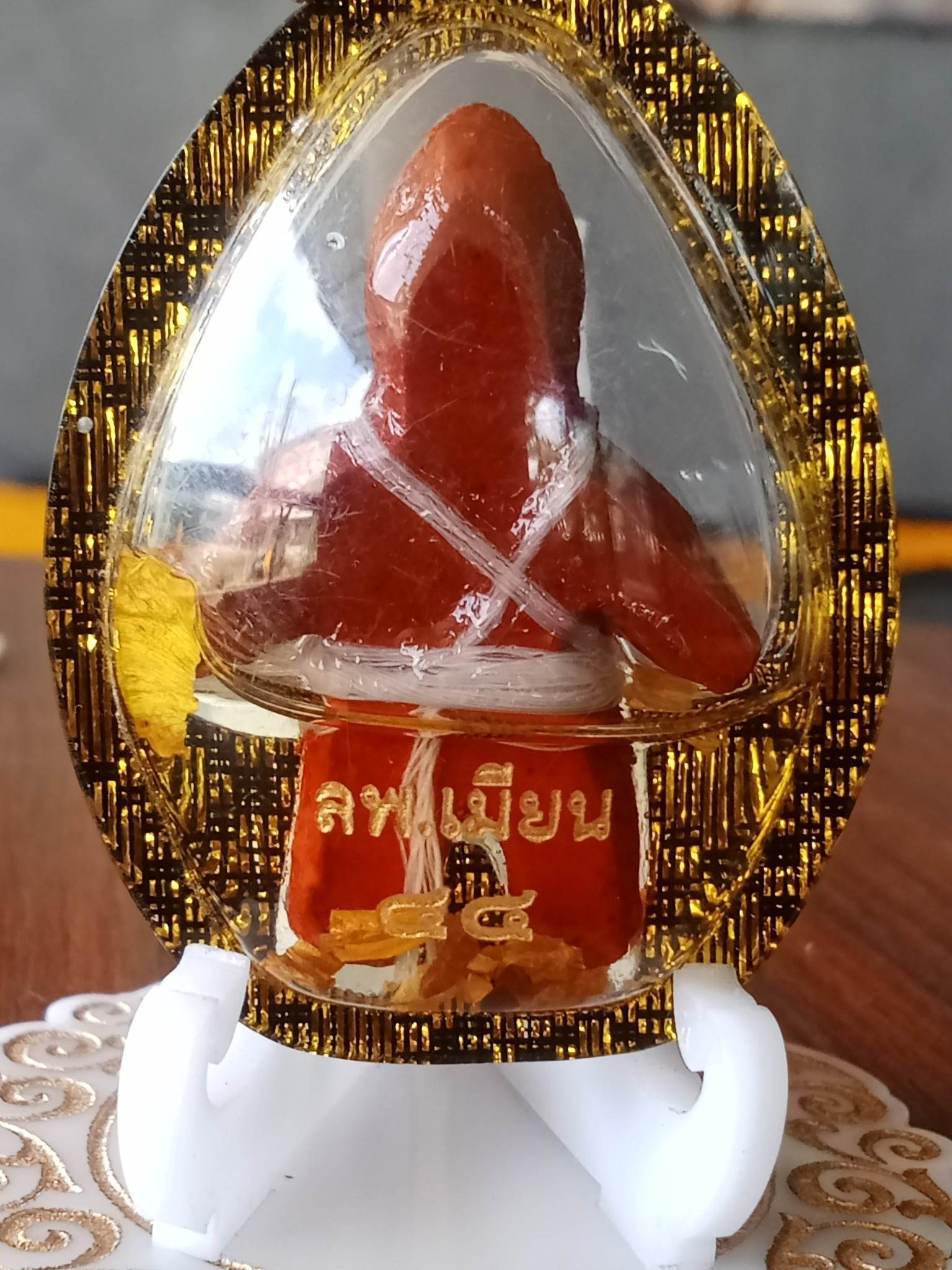 Oil-wrapped spirit doll for protection in a gold-trimmed clear casing on a white stand