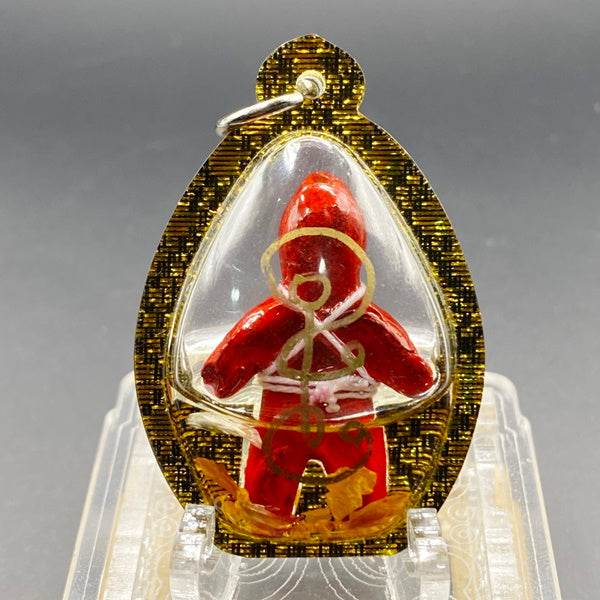 Thai Blessing Co oil-wrapped spirit doll for protection in gold-trimmed clear pendant with red doll figure