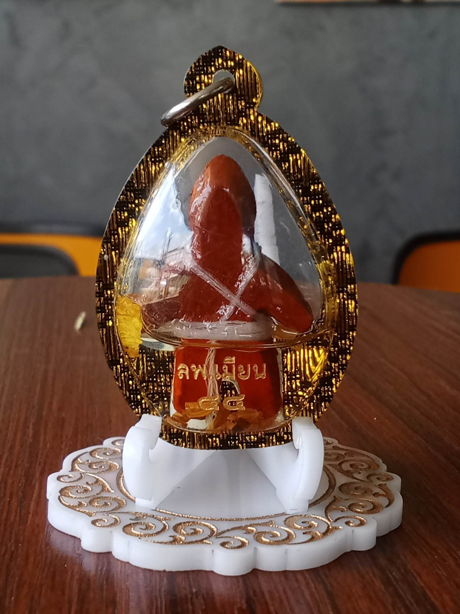 Oil-wrapped spirit doll for protection in a clear gold-trimmed amulet case on a decorative white stand