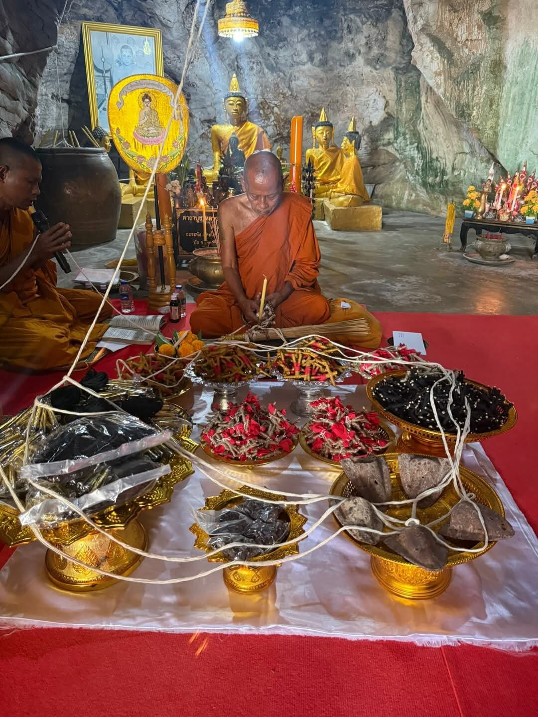 Monk performing ritual in cave temple blessing multiple amulet pendants on trays with cords blessed Thai Phan-Thai amulet for luck