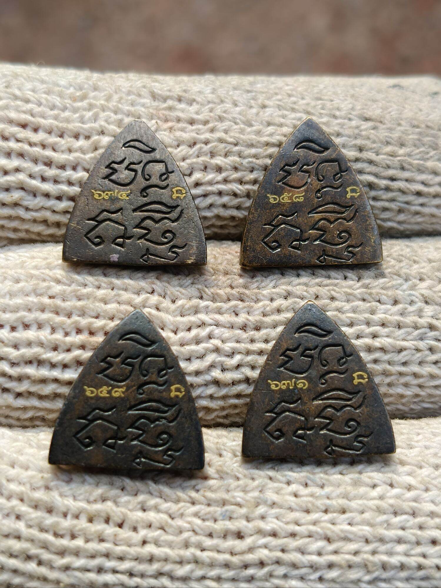 Four triangular metal Thai amulets with carved script and gold inlay on knit cloth blessed Thai Phan-Thai amulet for luck