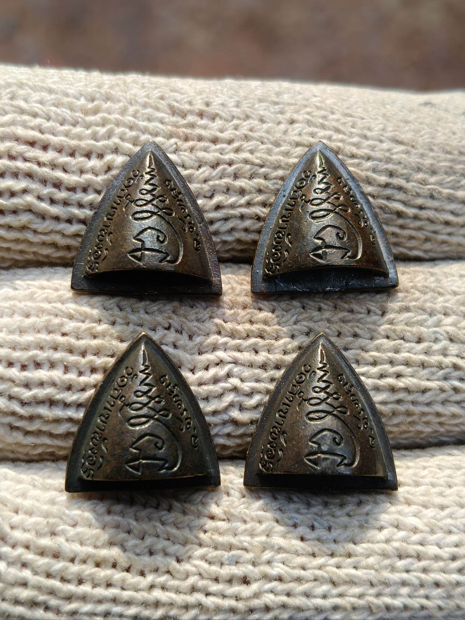 Four triangular dark metal amulet pendants with Thai script on knit background blessed Thai Phan-Thai amulet for luck