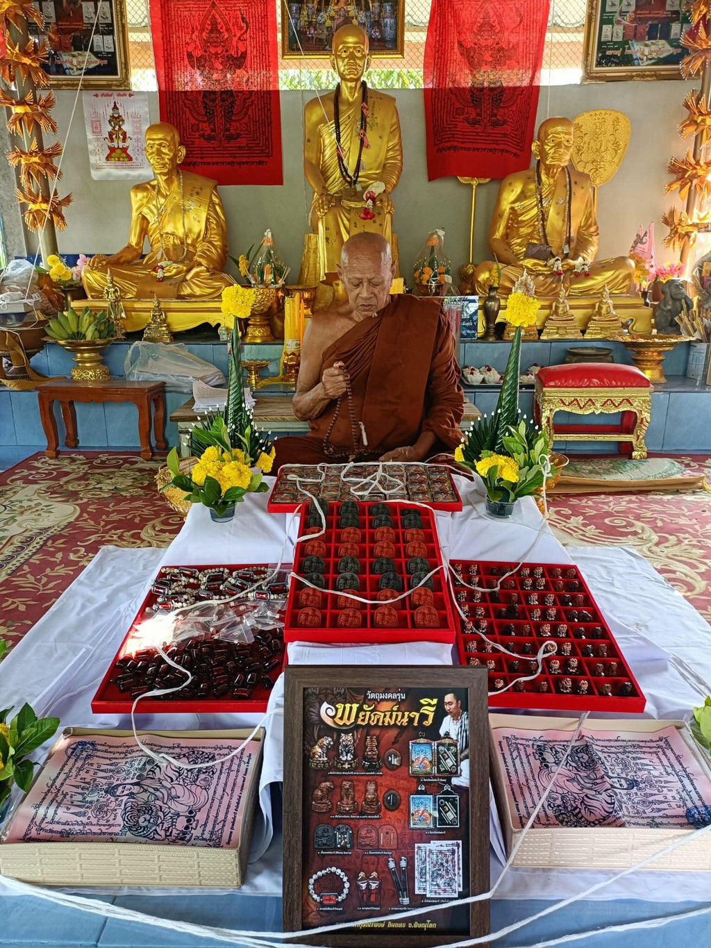 Phayak Naree tiger goddess amulet display on temple altar with monk seated gold statues and amulet trays