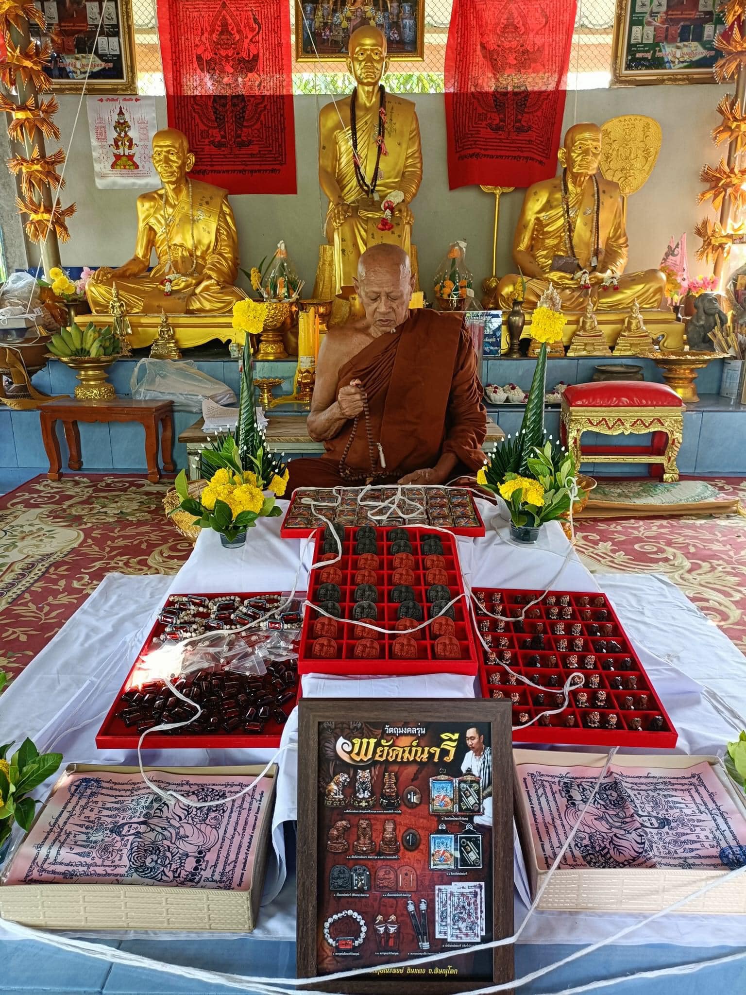 Phayak Naree tiger goddess amulet display on temple altar with monk seated gold statues and amulet trays