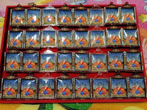 Red display tray of multiple Phayak Naree tiger goddess amulet pendants in gold frames with blue backgrounds