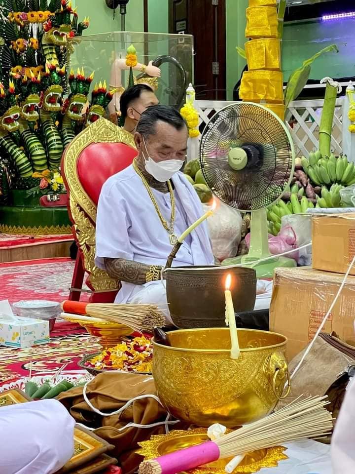 Ritual officiant in white blessing Phayak Naree tiger goddess amulet amid Thai temple offerings