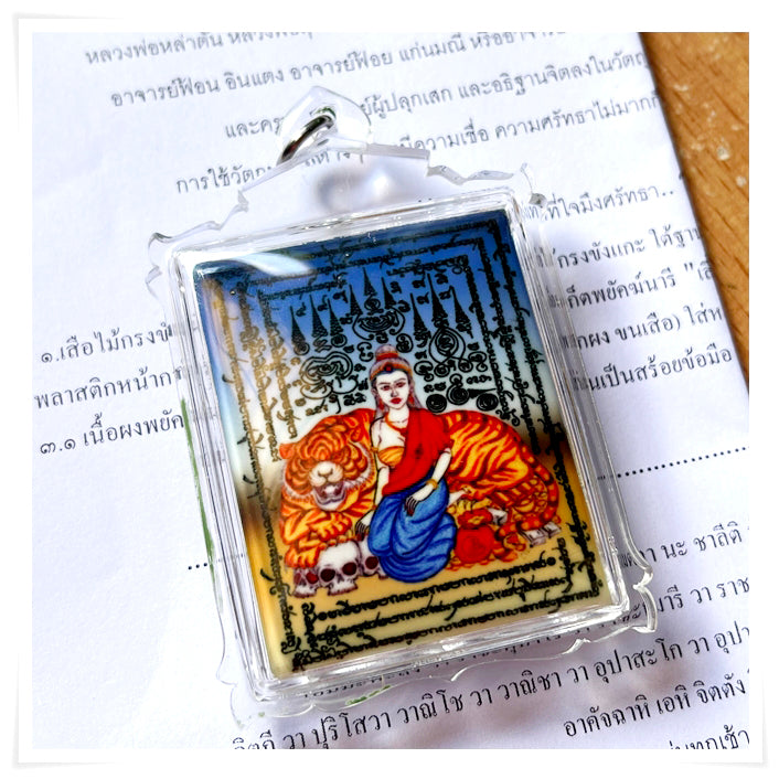 Phayak Naree tiger goddess amulet in clear plastic case showing colorful Thai deity seated on tiger with script background