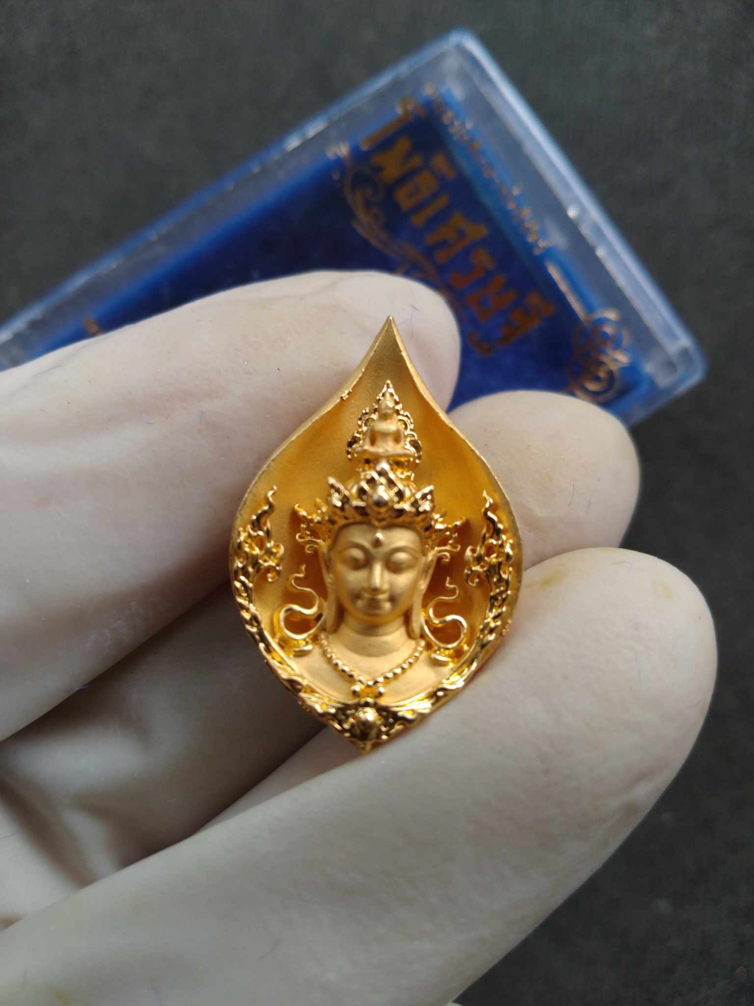 Avalokiteshvara Bodhisattva Phothi Setthi Edition gold amulet pendant held in gloved hand with ornate leaf design