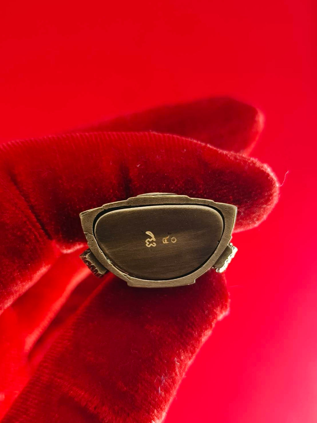 Close-up of Phra Buddha Chinnarat amulet held in a gloved hand against a red background