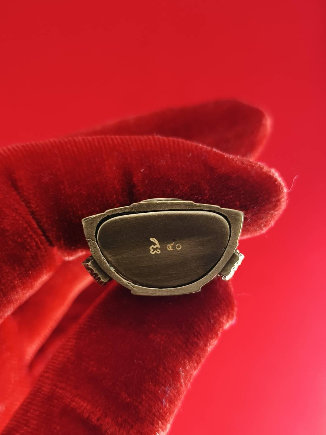 Close-up of Phra Buddha Chinnarat amulet held in a gloved hand against a red background