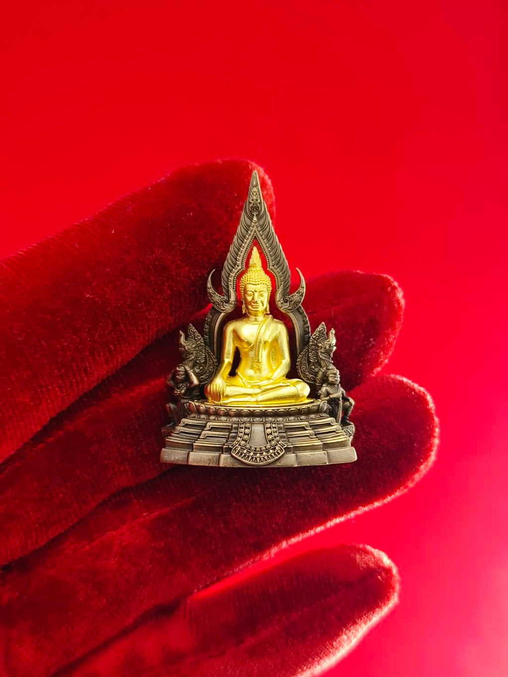 Phra Buddha Chinnarat amulet with intricate details in gold and silver on a red backdrop