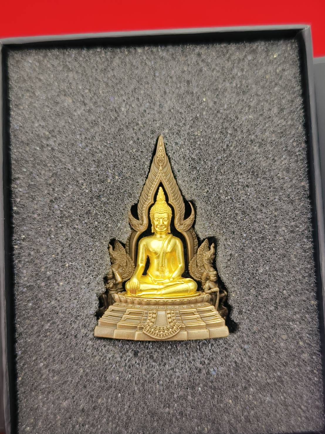 Phra Buddha Chinnarat amulet in gold and bronze with intricate detailing in a protective box