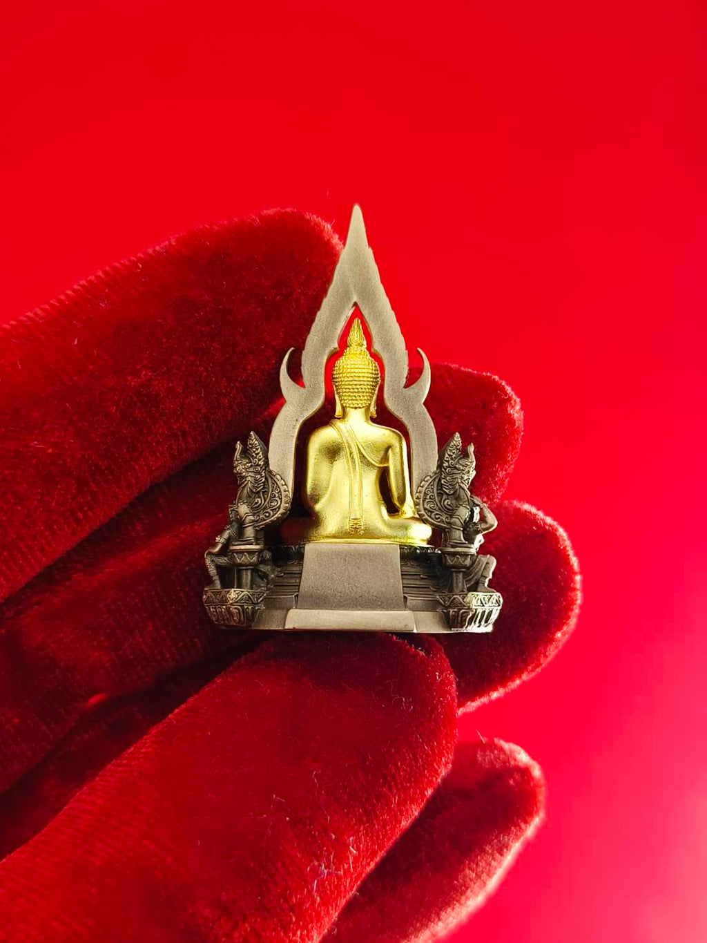 Phra Buddha Chinnarat amulet on a decorative base with intricate details held in a red glove