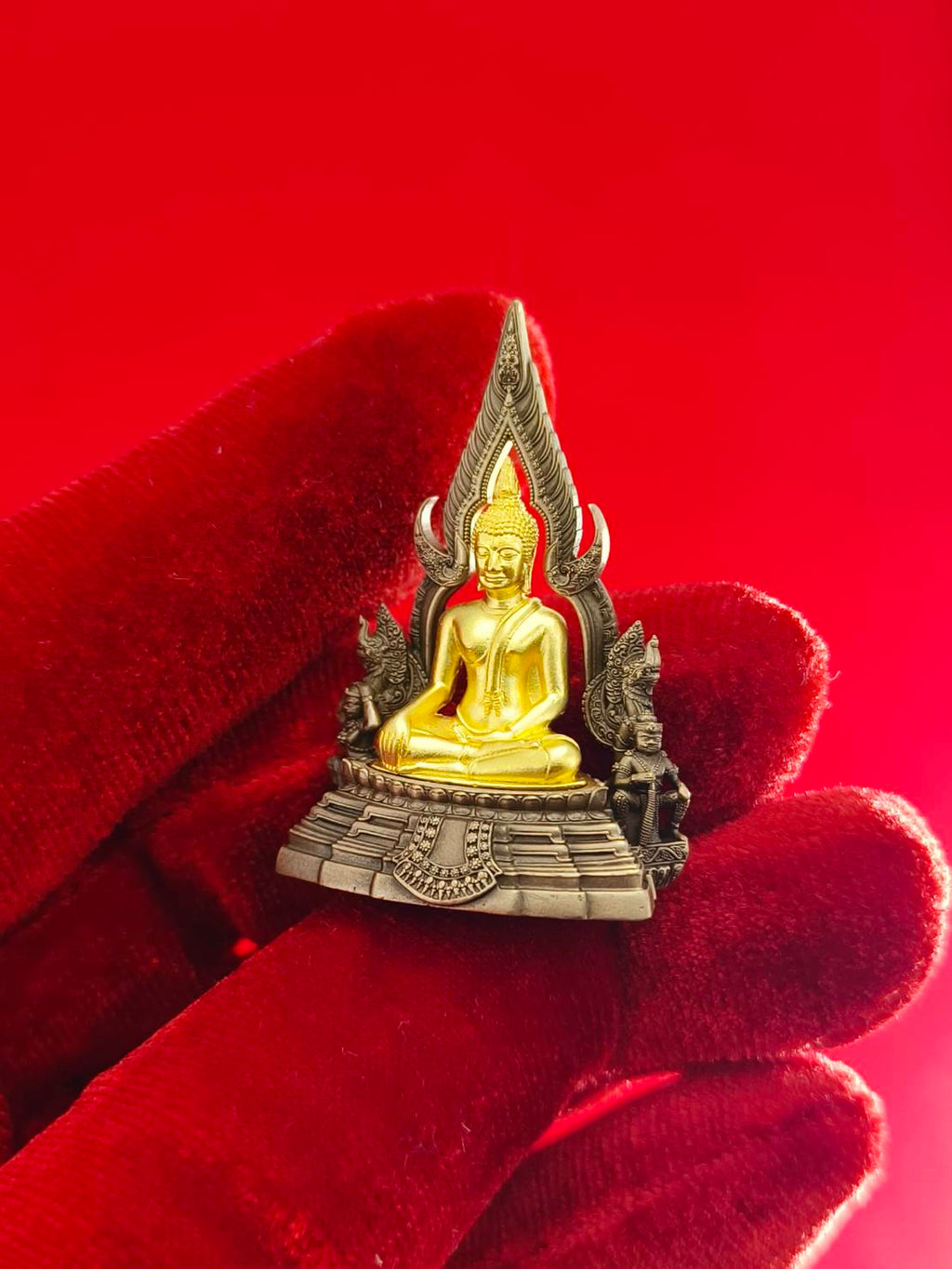 Handcrafted Phra Buddha Chinnarat amulet with intricate details, held against a red background