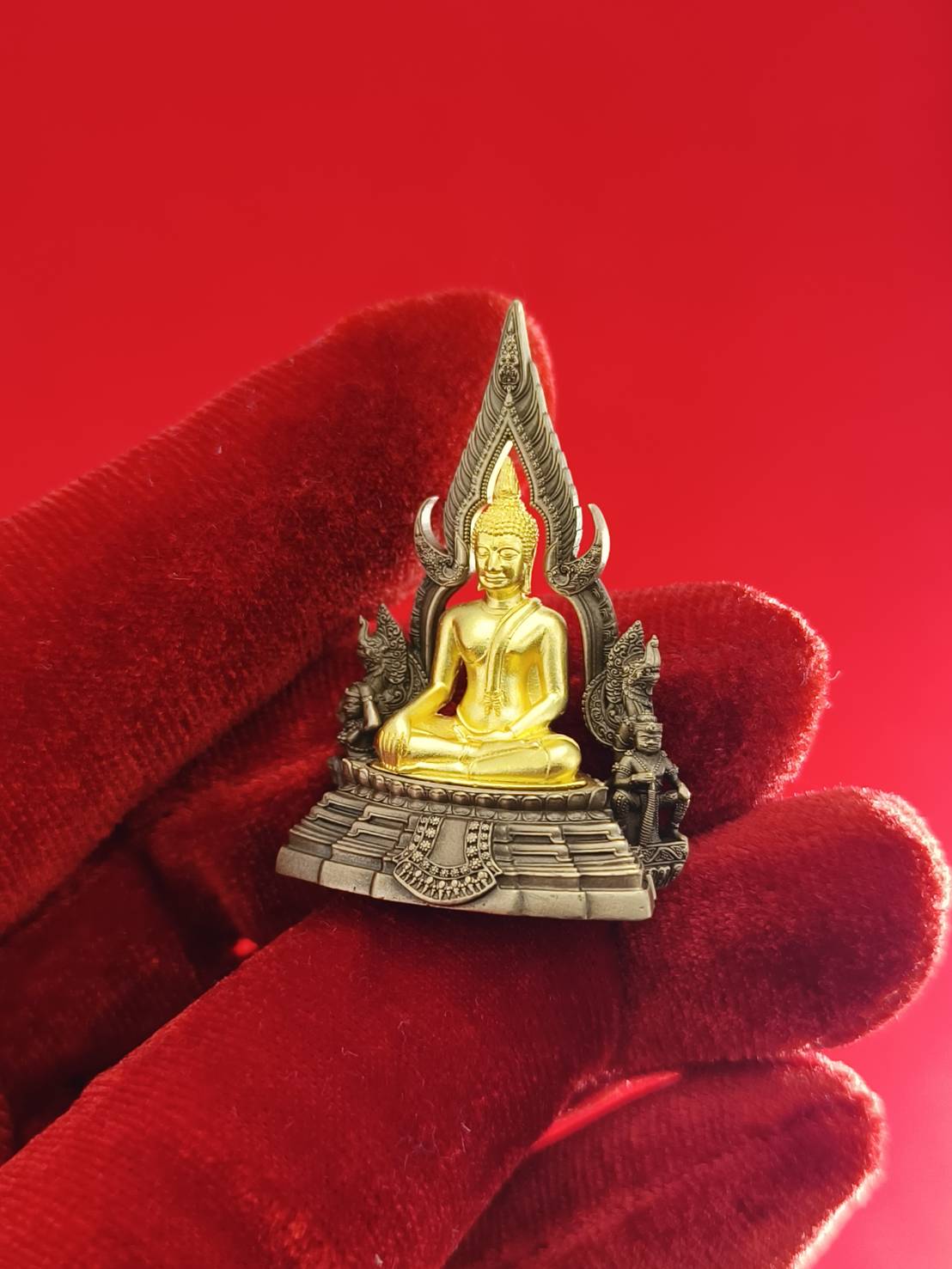 Handcrafted Phra Buddha Chinnarat amulet with intricate details, held against a red background