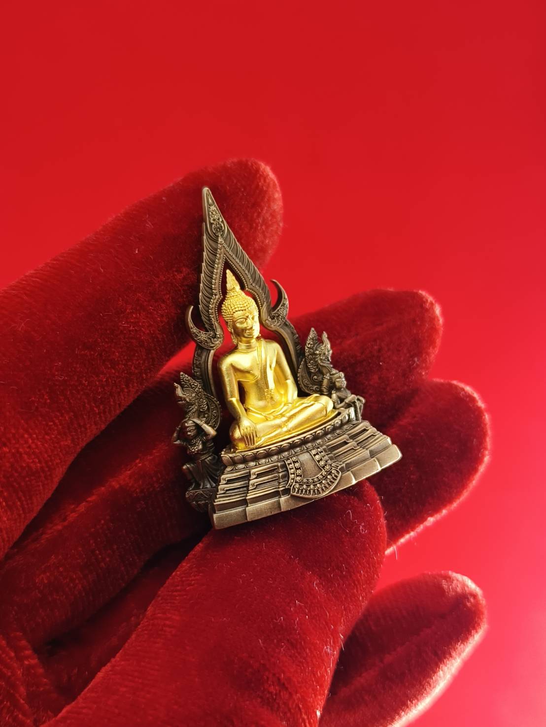 Phra Buddha Chinnarat amulet with intricate details on a red background, ideal for home decor and spiritual ambiance