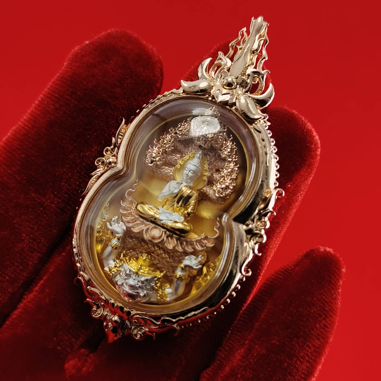 Phra Naga Prok amulet for protection in ornate gold casing held against a red background