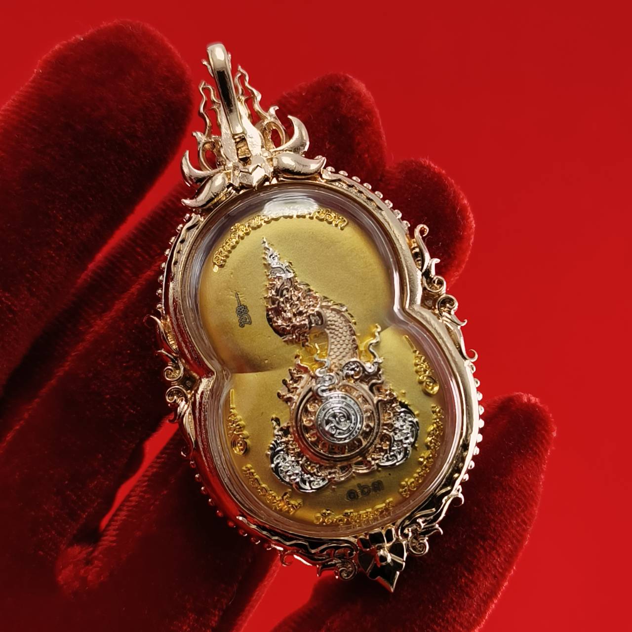 Phra Naga Prok amulet for protection in ornate gold casing, held against a red background