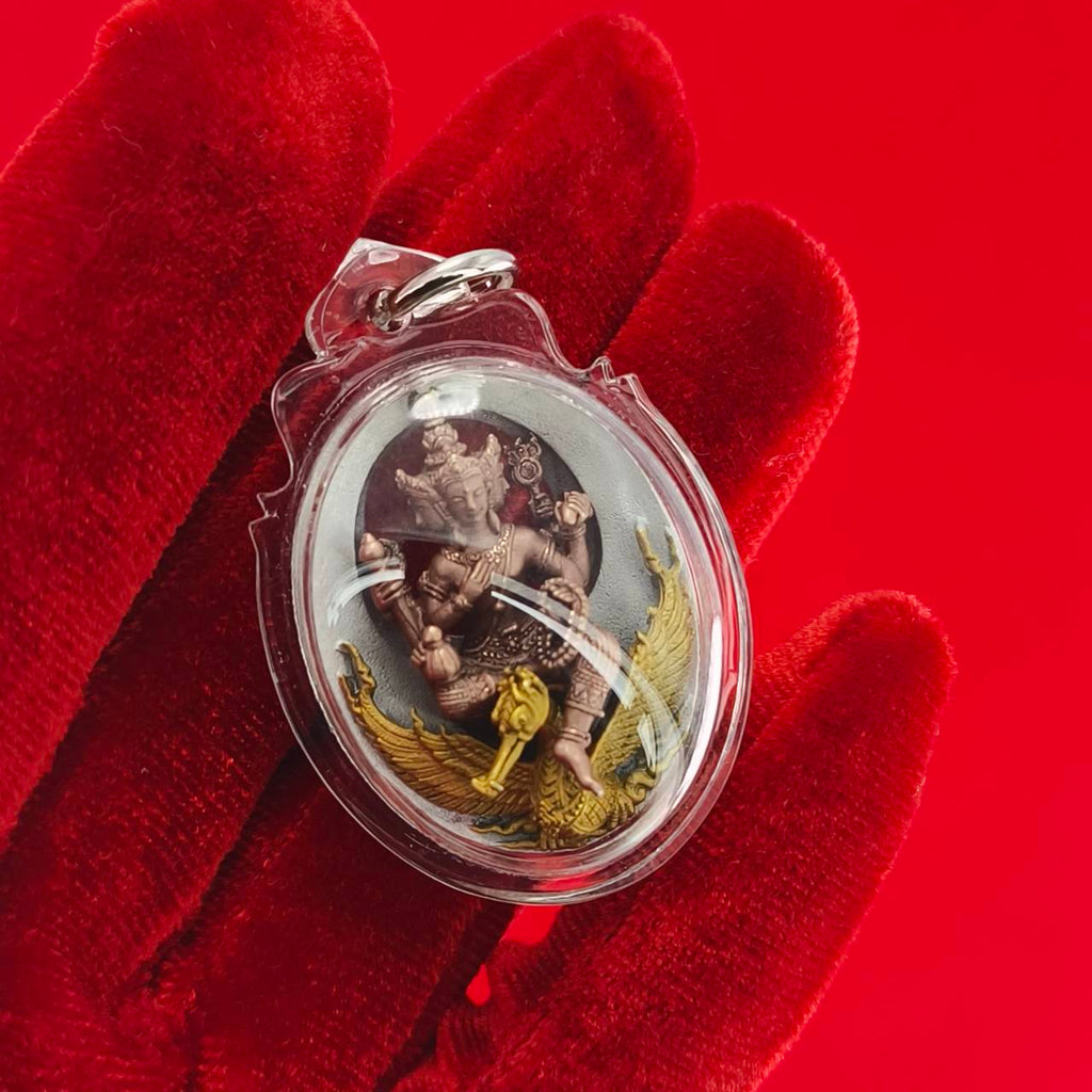 Phra Phrom Thai amulet in a clear pendant held by a red-gloved hand, symbolizing protection and blessings