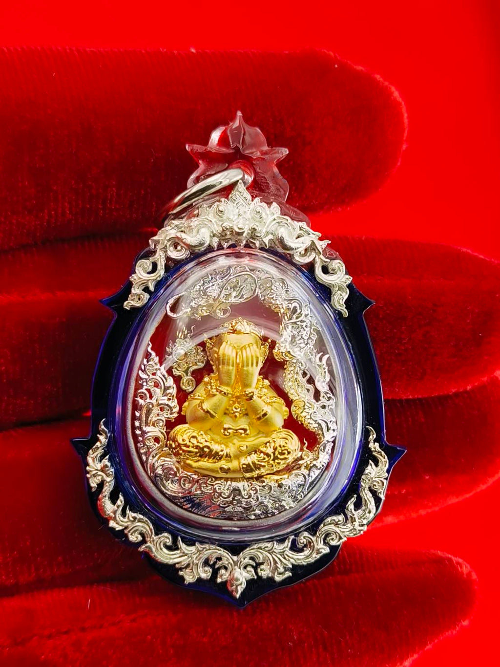 Phra Pidta amulet for wealth in an ornate silver frame against a red background