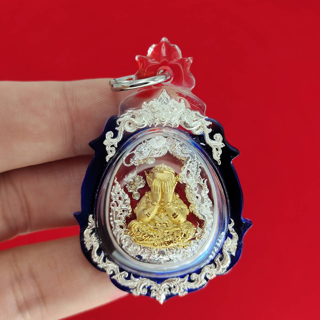 Phra Pidta amulet for wealth encased in a decorative clear pendant with intricate details