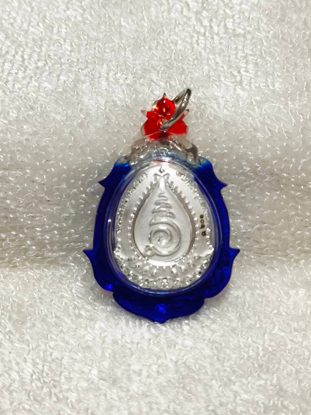 Phra Pidta amulet for wealth encased in a blue and silver pendant with decorative details