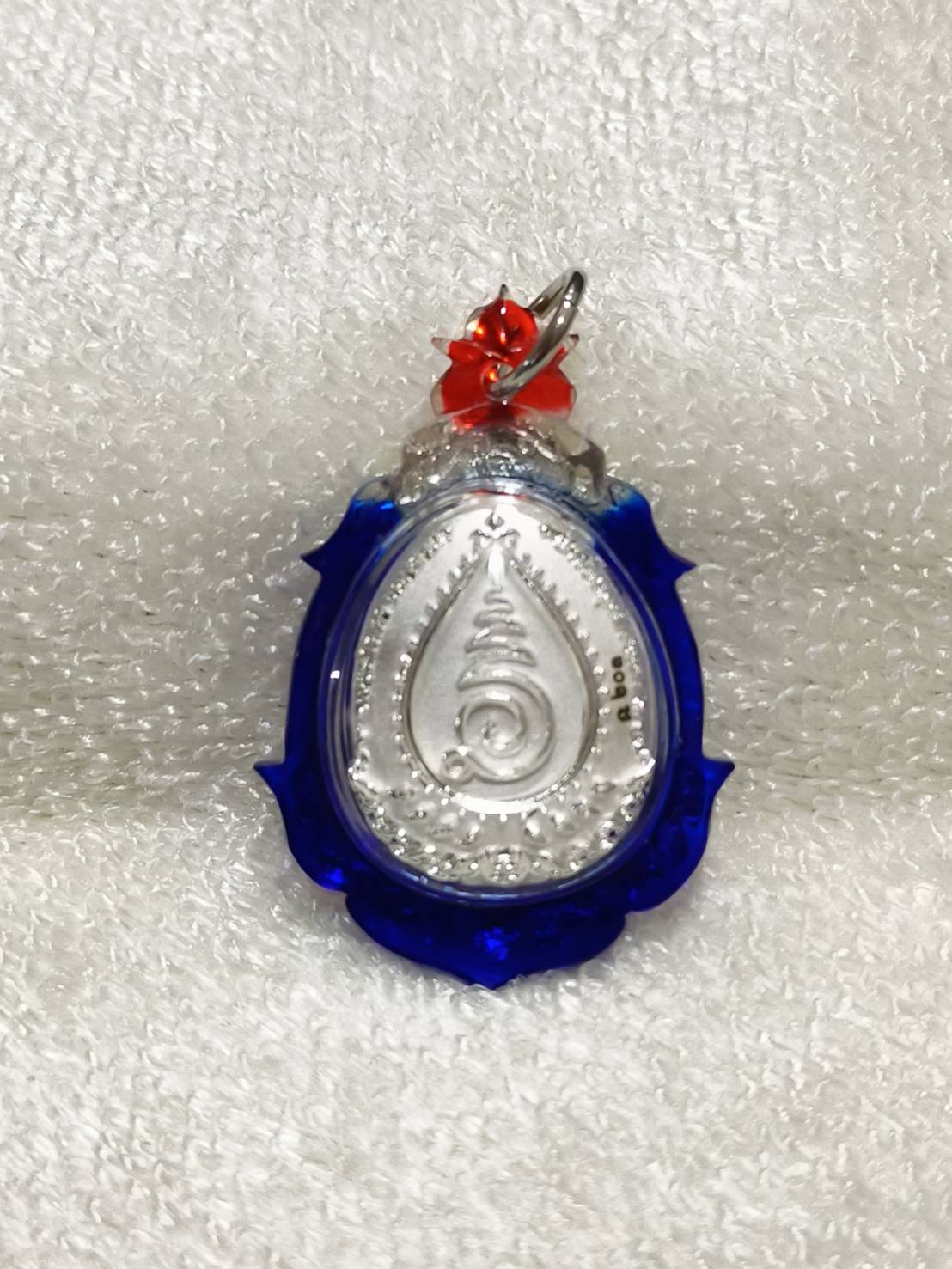 Phra Pidta amulet for wealth encased in a blue and silver pendant with decorative details