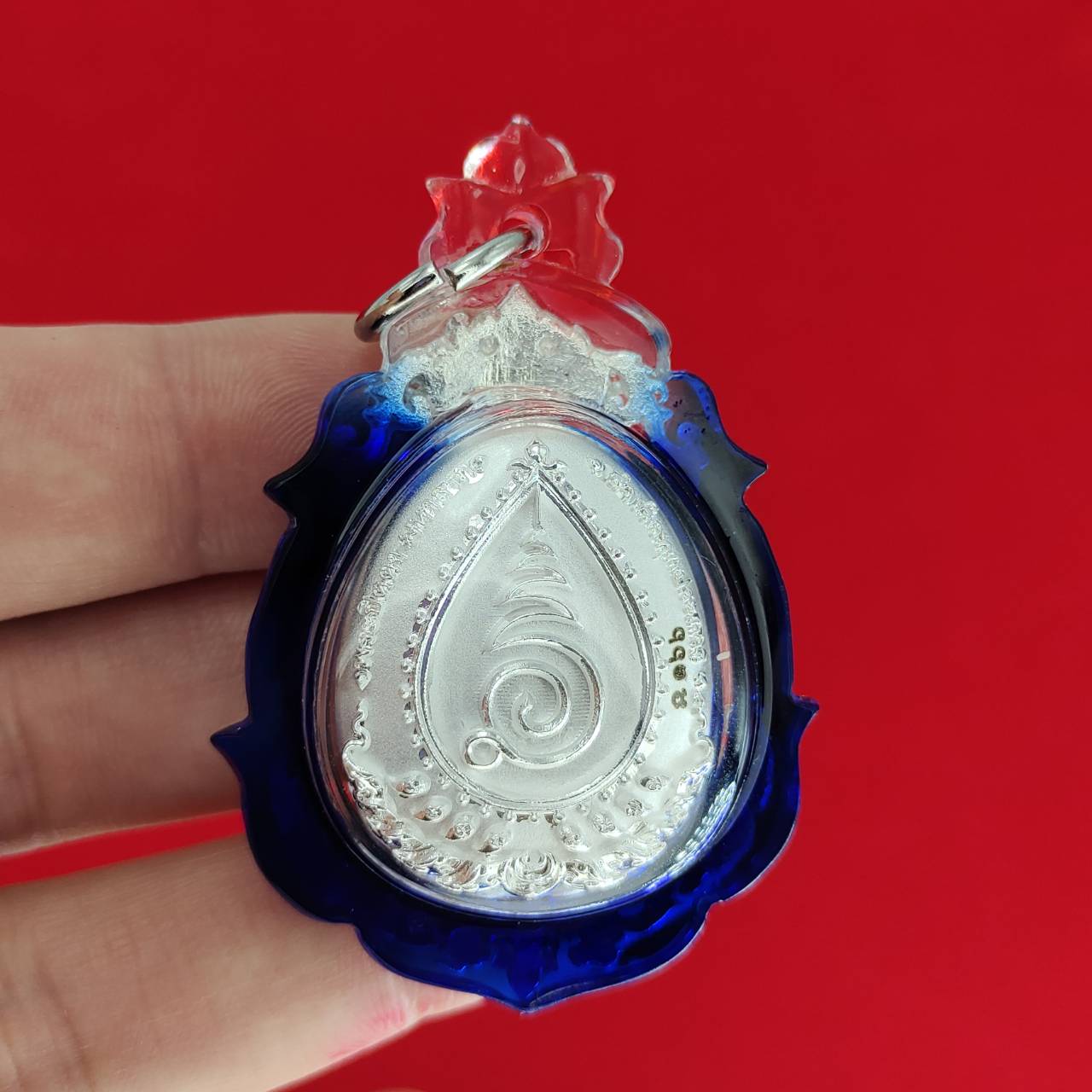 Phra Pidta amulet for wealth in a decorative blue and clear casing, perfect for collectors