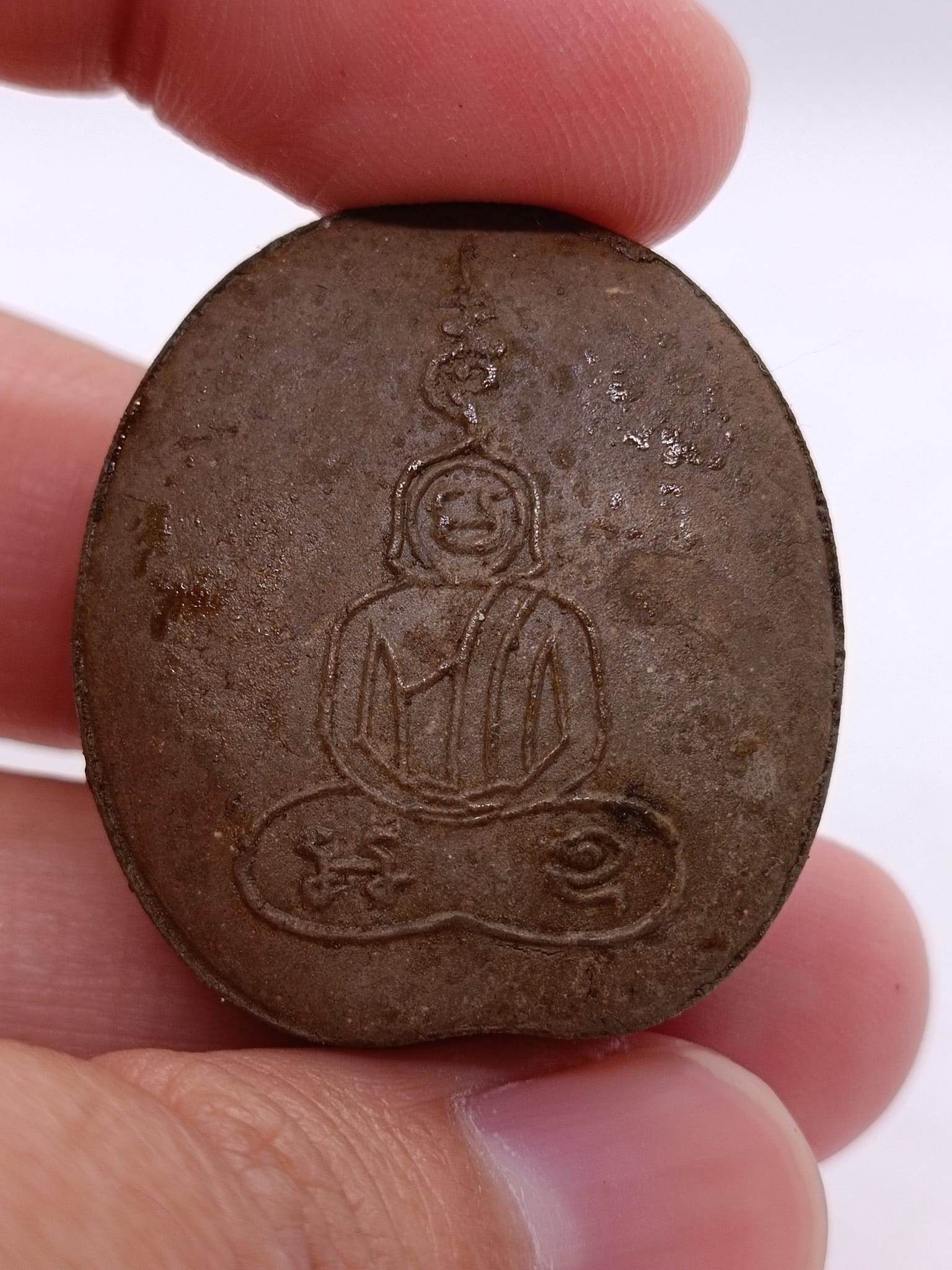 Phra Pidta wealth amulet with detailed engraving of Buddha figure held between fingers