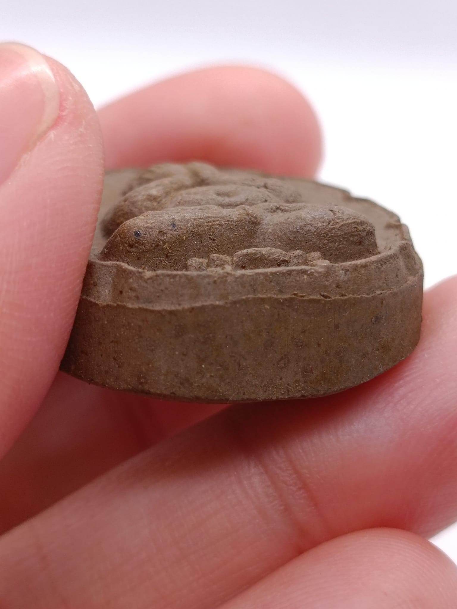 Phra Pidta wealth amulet held in hand, showcasing its detailed craftsmanship and texture