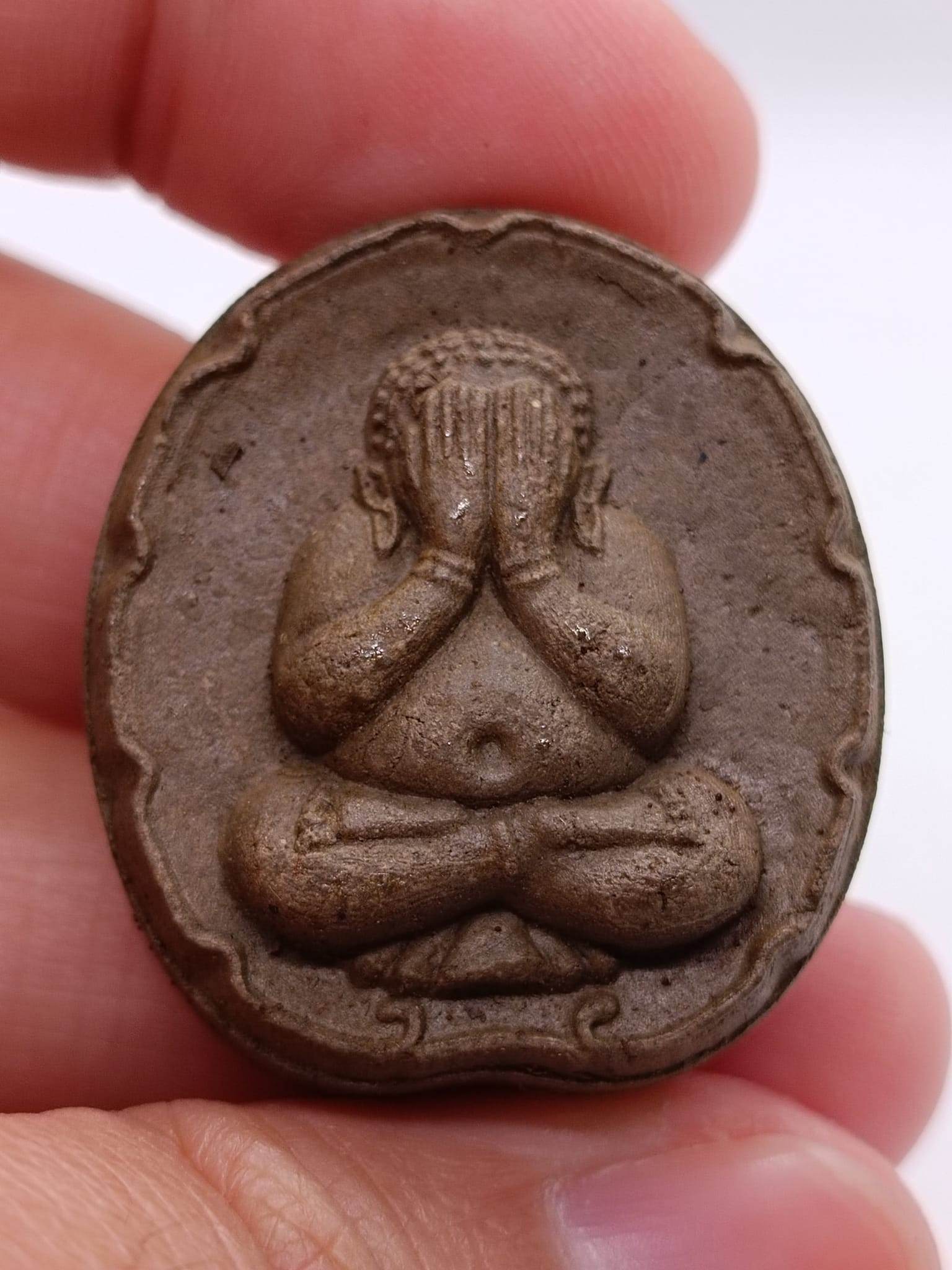 Phra Pidta wealth amulet featuring a seated Buddha with hands over eyes for prosperity and good fortune