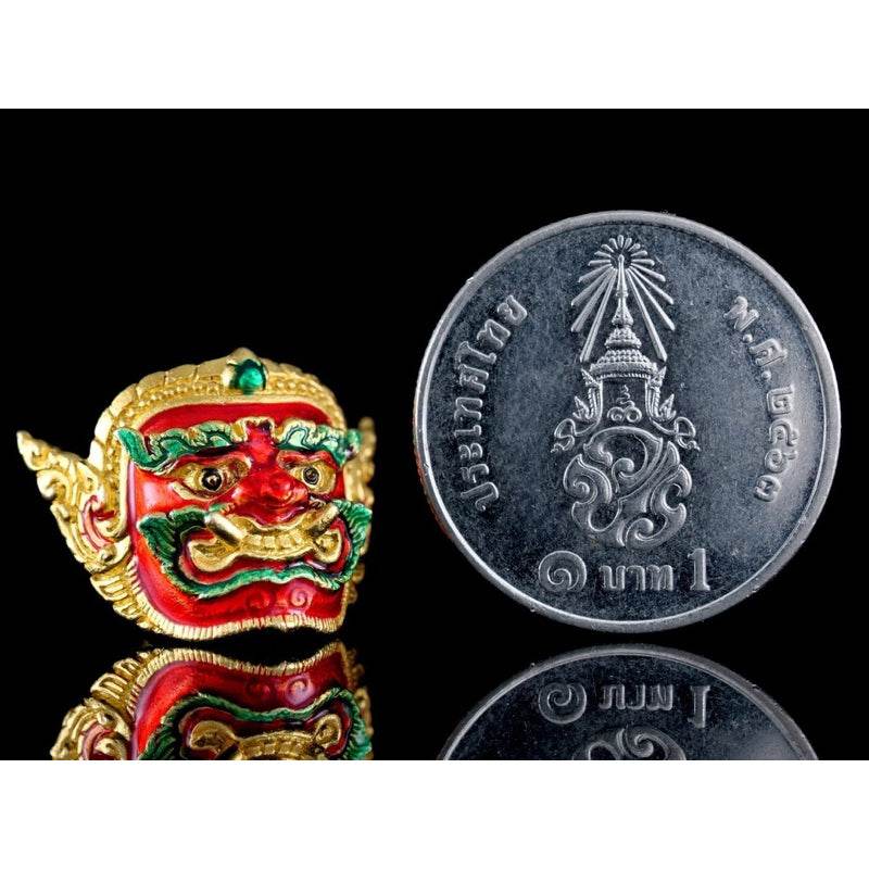 Colorful Phra Pirap amulet for power displayed next to a coin for size comparison