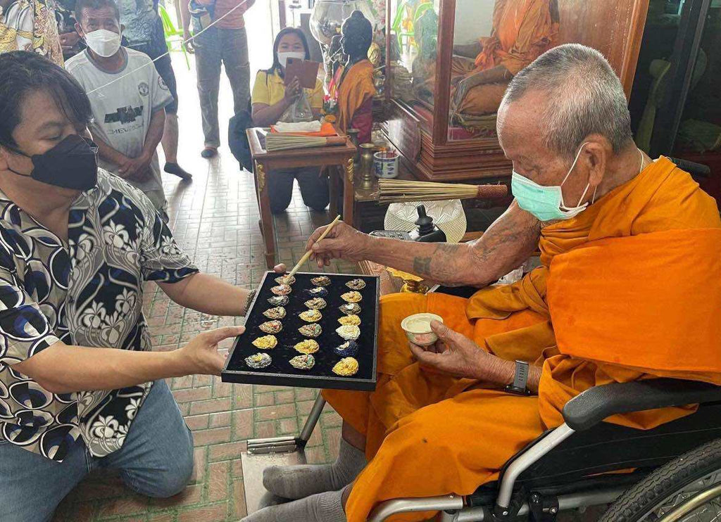 Phra Sangkajai and Phra Upakut amulet display during a traditional blessing ceremony by a monk