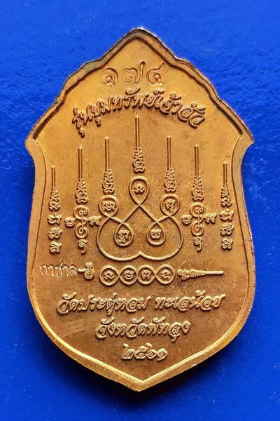 Gold Phra Siwali amulet for wealth with intricate Thai inscriptions on a blue background