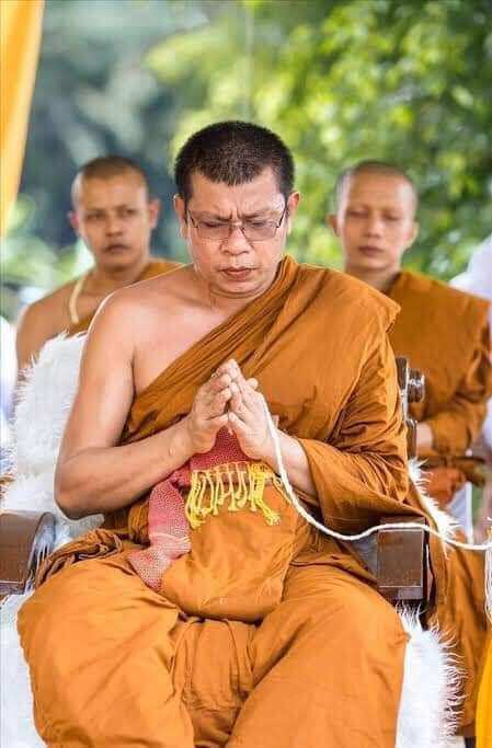 Buddhist monk meditating wearing traditional robes with Phra Siwali amulet for wealth