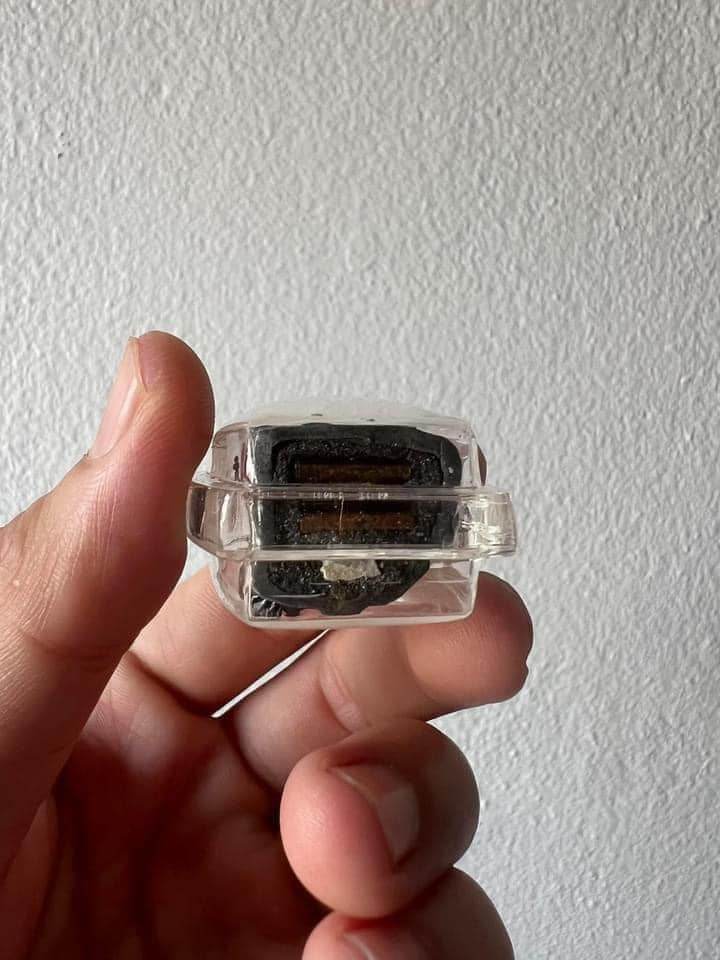 Hand holding a Phu Chao Saming Phrai spirit figurine encased in a clear protective box