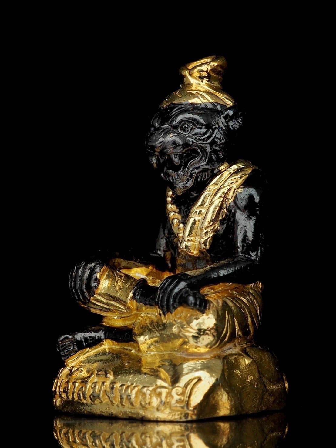 Black and gold Pu Jao Saming Prai spirit talisman statue with intricate detailing on a reflective surface