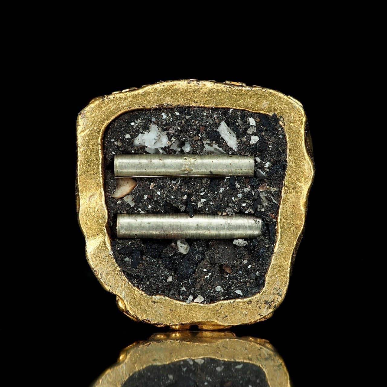 Close-up of Pu Jao Saming Prai spirit talisman with gold frame and embedded metal rods on black background