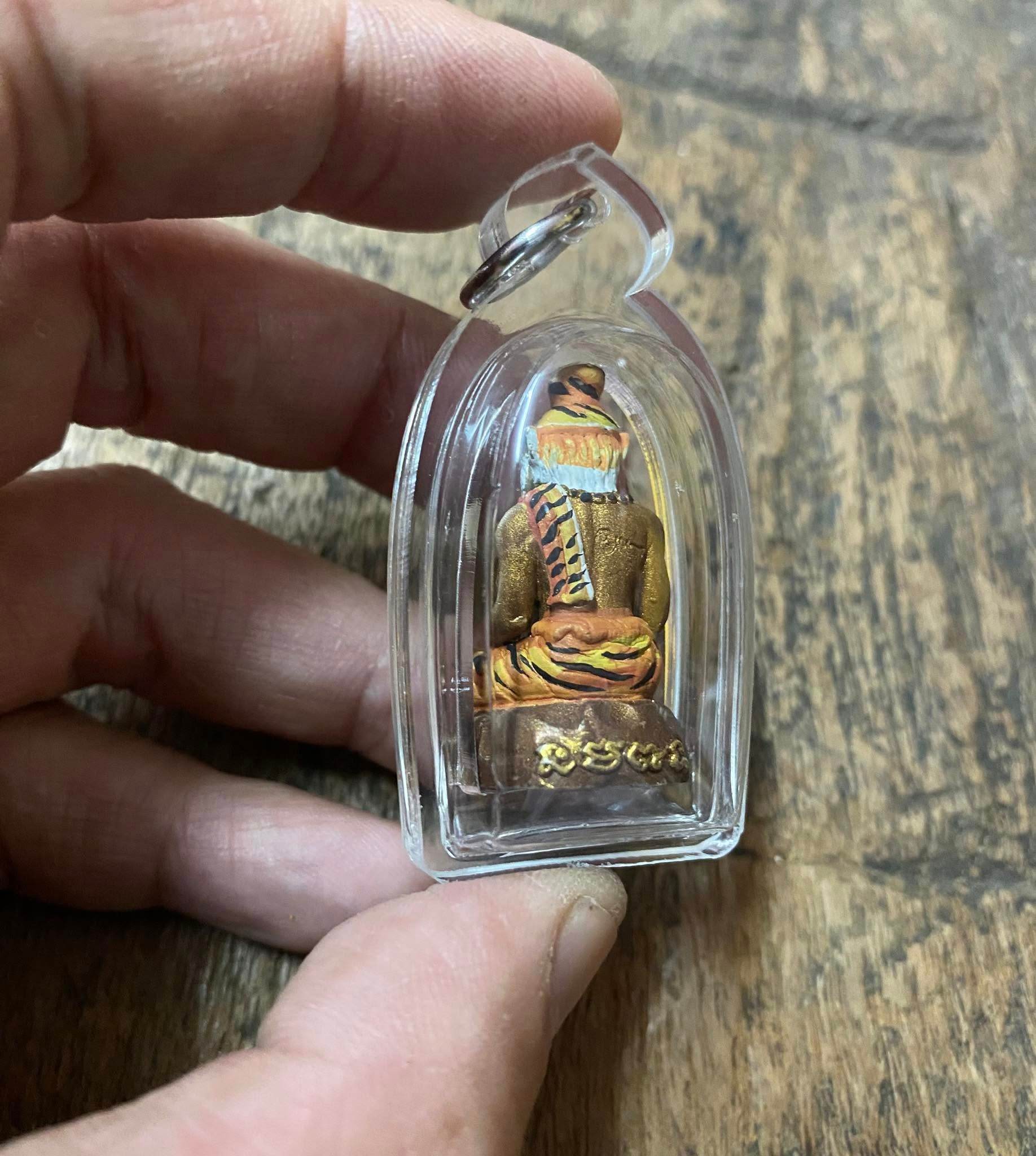 Hand holding Pu Jao Saming Prai spirit talisman in clear protective casing on wooden surface