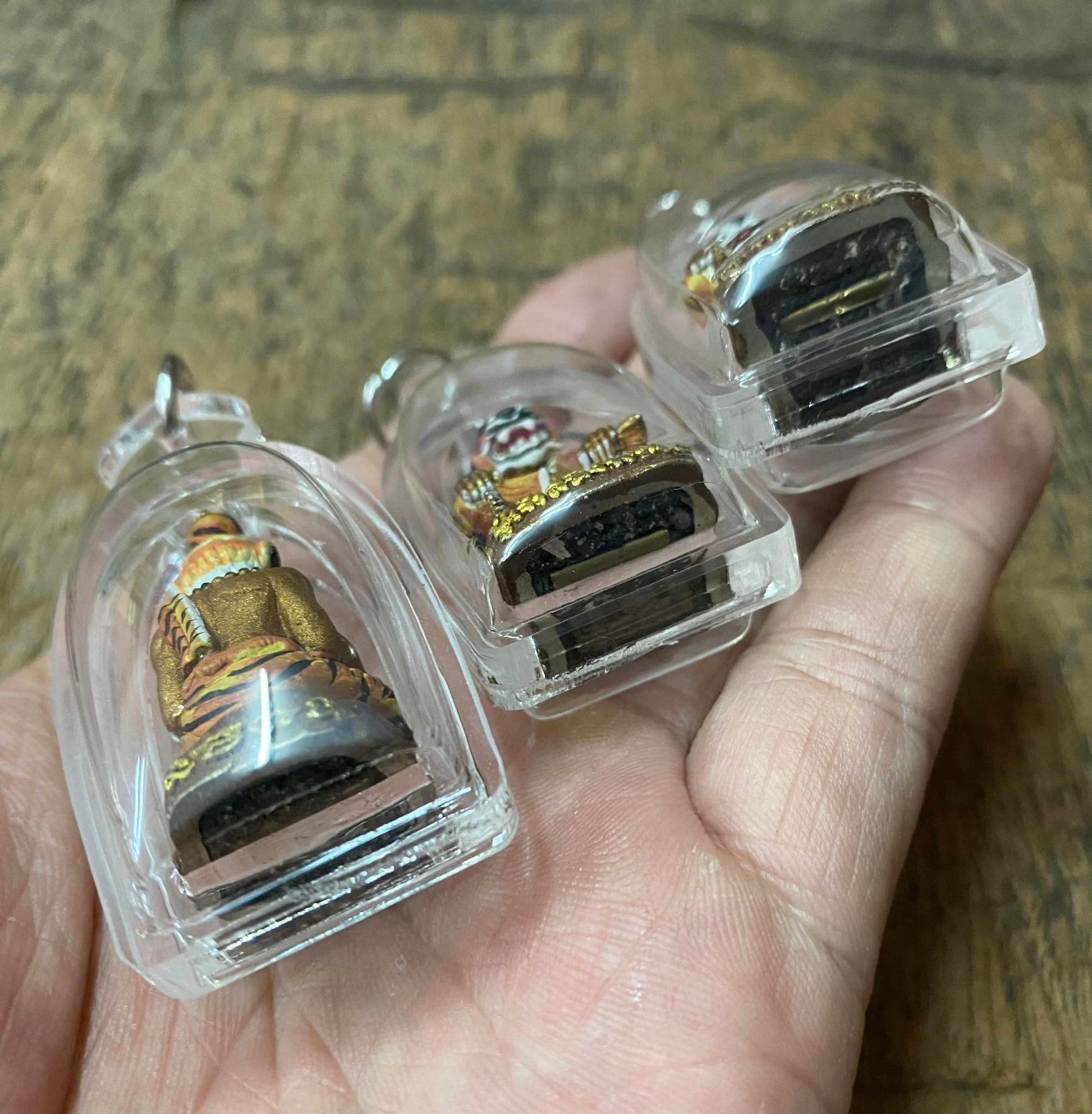 Hand holding three Pu Jao Saming Prai spirit talisman amulets in clear protective cases from Thai Blessing Co