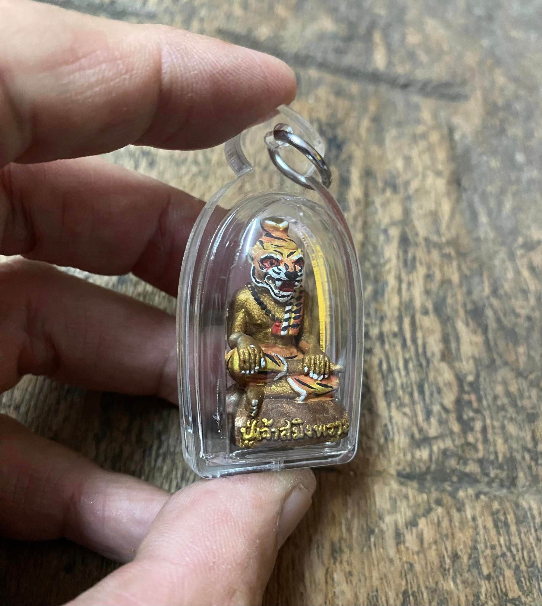 Hand holding Pu Jao Saming Prai spirit talisman encased in clear plastic from Thai Blessing Co