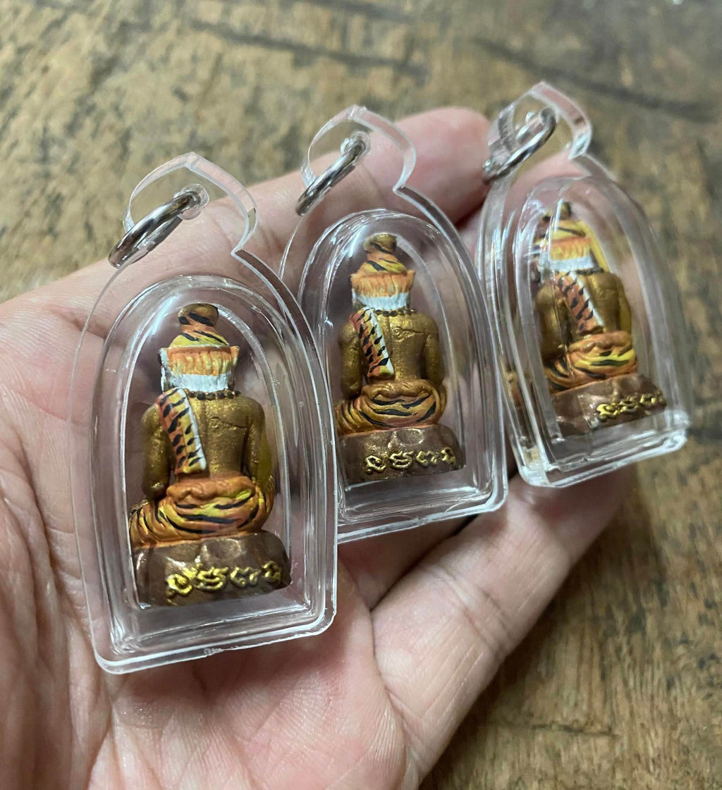 Hand holding three Pu Jao Saming Prai spirit talisman amulets encased in clear protective covers