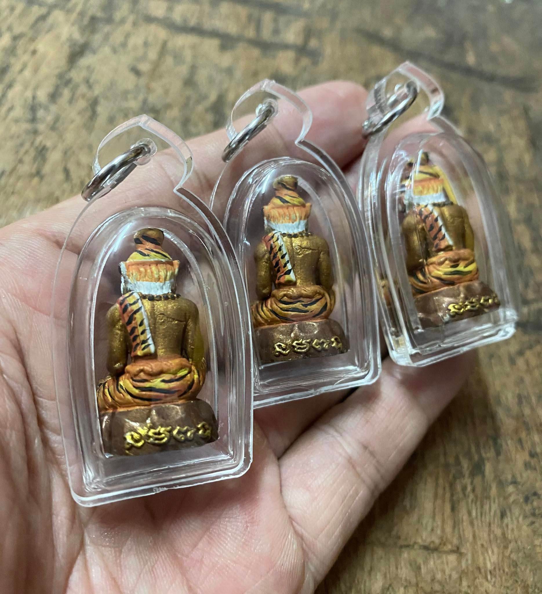 Hand holding three Pu Jao Saming Prai spirit talisman amulets encased in clear protective covers