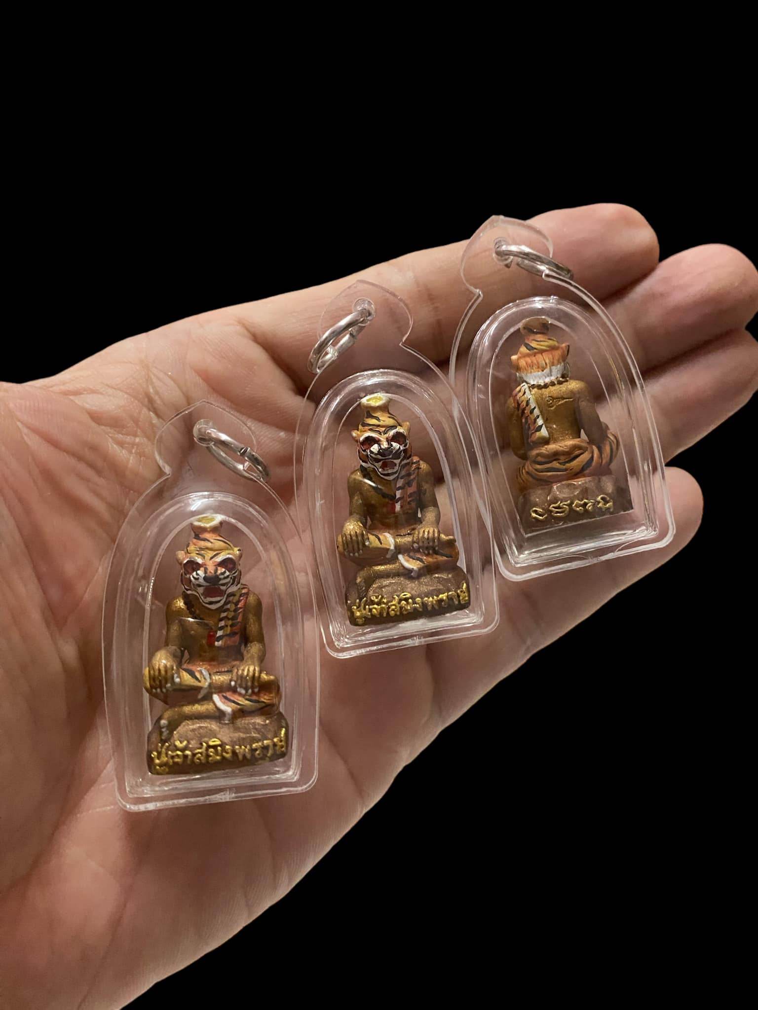 Three small Pu Jao Saming Prai spirit talisman figures in clear protective cases held in a hand